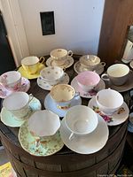 Top view of 12 vintage teacups on saucers arranged on round table showing variety of colors and patterns