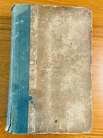 Top front cover of 1828 British Essayists Vol.5 showing worn beige boards with blue cloth spine frayed and torn at edges.