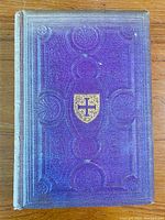 Front cover of the book showing purple embossed cloth with gold shield emblem in center and decorative circular patterns.