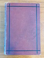 Front cover of the book showing reddish color with black rectangular lines as decoration, spine with wear.