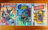 Four Justice League of America comic books front covers displayed, showing vibrant illustrations and logos featuring various DC superheroes.