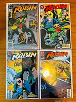 Four Robin comic books laid out on a wooden surface showing covers of issues #2, #13, #15, and one unidentified issue.