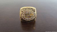 Top view of the gold-tone replica Super Bowl ring with simulated diamonds and 'WORLD CHAMPIONS' lettering visible.