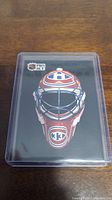 Front view of the Patrick Roy hockey card featuring the illustrated goalie mask of the Montreal Canadiens on black background, in protective plastic casing.