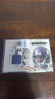 Front view of Randy Moss football card numbered 16/75 with autograph and embedded jersey piece, placed on wood background.