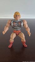 Front view of vintage 1980s MOTU Battle Armor He-Man action figure showing muscular build, silver chest armor with battle damage, orange shorts, and red boots.