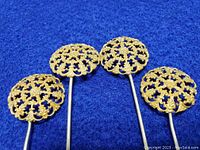 Four ornate filigree dome gold-tone hat pins laid on blue fabric, showing detailed craftsmanship and size.