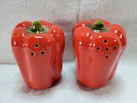 Front and angled view of the two red bell pepper salt and pepper shakers showing the holes on top for dispensing.