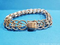 Silver charm bracelet laid flat showing full length and design of interlinked twisted oval loops and box clasp stamped GB and sterling.