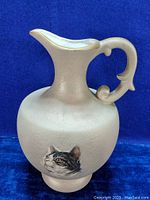 Full view of light beige/sand textured ceramic ewer jug with cat decal and gold painted handle and spout rim.