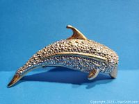 Side view of the dolphin brooch showing the silver-tone textured body, gold-tone fins, tail, and beak, and the green eyes detail.