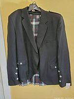 Full view of black Scottish dress blazer on a hanger showing front, silver buttons on pockets and sleeves, and tartan lining inside.