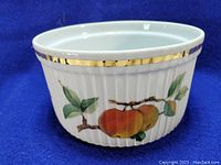 Front side of white ceramic Royal Worcester Evesham bowl with vertical ridges, gold rim and peach fruit decoration.