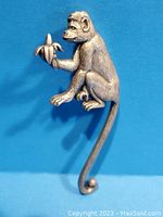 Front view of the detailed pewter monkey brooch holding a peeled banana against a blue background.