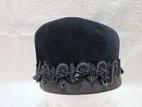 Front view of black velvet pillbox hat showing rounded crown and ribbon band at the base
