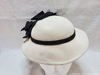 Front view of cream wool ladies tilt hat with black ribbon band and bow.