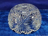 Clear vintage cut glass bowl showing intricate pinwheel and star patterns on the bottom, placed on a blue velvet background.