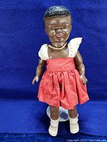 Full front view of vintage Dee Cee doll standing against a blue background showing red dress, pearl necklace, and white boots.