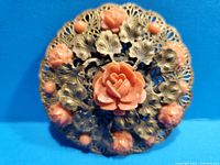 Close-up of vintage brooch showing central coral-colored carved rose surrounded by smaller roses with detailed filigree metal background.