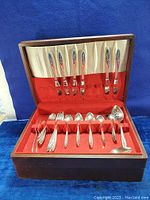 Full open wooden canteen chest displaying knives in the upper section and other silverware in the lower drawer lined with red felt.
