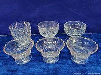 Photo of six vintage sherbet dessert glass footed bowls of various sizes on a blue velvet background. Clear glass, different patterns including geometric, ribbed, bubble textures.