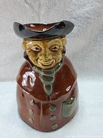 Frontal view of the redware toby jug showing the colonial man's facial features, tricorn hat, and front of the coat with buttons and pocket.
