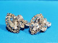 Front angled view of the pair of vintage Sherman rhinestone clip earrings showing clear crystals and silver-tone scalloped setting.