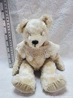 Front view of the beige vintage teddy bear with lace shawl, sitting upright with a ruler beside showing about 10 inches tall.