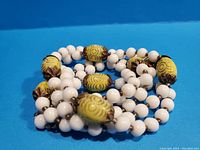 Close-up photo showing details of yellow glass beads with intricate gold and brown filigree caps along with smooth white round beads.