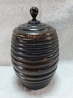 Front view of barrel-shaped dark wooden humidor with lid and knob handle on top, showing ribbed texture and surface wear.