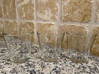 Front view of three clear glass dessert or short cocktail glasses on a granite countertop with beige tiled wall.