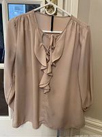 Front view of beige chiffon blouse hanging on hanger, showing ruffled V-neck with front tie and 3/4 length sleeves.