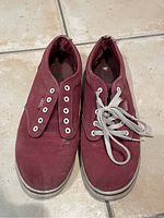Photo of burgundy women's Vans shoes, size 7, slip-on style with white eyelets and white rubber soles. One shoe has tied grayish laces, the other shoe has no laces. Shoes show signs of wear and dirt marks on sole, suitable for gardening or yard work as per seller.