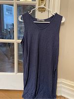 Navy blue sleeveless tunic shirt hanging on a hanger in front of glass door.