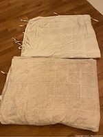Folded weighted blanket with fluffy cream sherpa faux fur fabric on one side and a flat cream fabric cover with tie strings on the other side lying on hardwood floor.