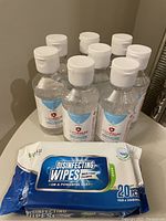 Eight bottles of Canpalm hand sanitizer and one pack of VuKu disinfecting wipes on a white surface.