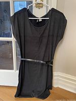 Front view of little black dress hanging on a hanger, showing rounded neckline, short dolman sleeves, and attached thin black belt at waist.