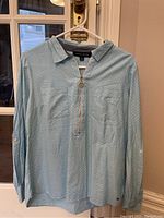 Front view of the Tommy Hilfiger long sleeve sky blue polka dot top hanging on a hanger, showing two chest pockets and collar