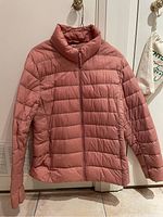Front view of salmon-colored Uniqlo ultralight down jacket hanging on a hook, zipped closed