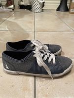 Side view of left and right navy blue boat shoes with white laces and sole, on tile floor