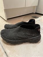 Side angle photo showing the profile of the black woven slip-on shoes with thick rubber sole.