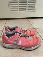 Side view of pair of coral Nike sneakers showing pink and coral mesh upper, white Nike swoosh and white sole with signs of dirt and wear.