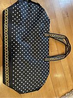 Full view of black overnight bag with white polka dots and gold chain printed pattern on handles and bottom trim, showing overall design and size.