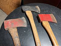 Three axes placed on a black table showing the metal heads and wooden handles.