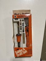 Front view of unopened Black & Decker Solder & Craft Set in original orange and white box showing soldering iron, stand, solder, and tips.