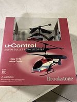 Front packaging showing Brookstone uControl Silver Bullet RC Helicopter in red and silver with clear window display and product branding.