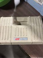 Closed beige plastic carrying case of Coleman Inflate-All 150 inflator with label on top.