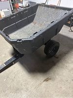 Front angled view of the black plastic hauling cart with visible dirt inside the bed and front axle with tires.