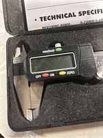 Electronic digital caliper screen and control buttons close-up showing mm/inch toggle, OFF, ON and ZERO buttons in black plastic body within foam case.