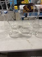 Four clear glass KiMax lab glass receptacles on a white table with a football helmet and other items in background.